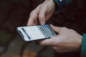Close-up of two hands holding a smartphone and typing on its on-screen keyboard.