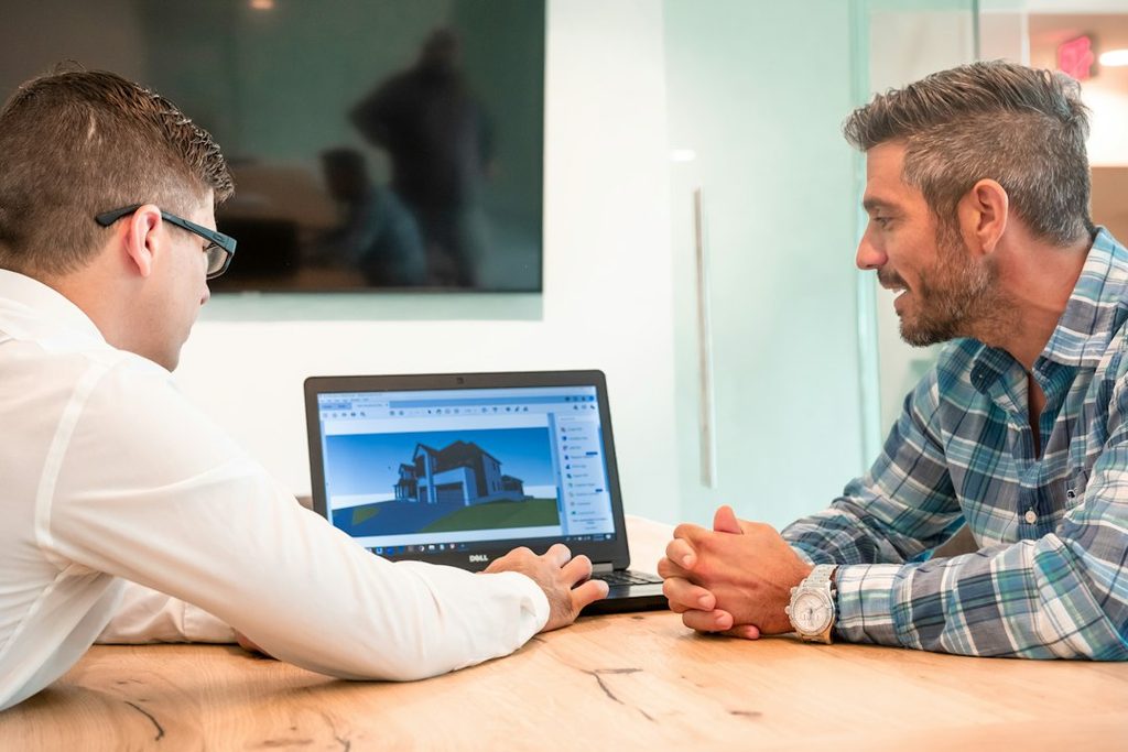 Two colleagues, designer and developer, sit at a table and review work on a laptop together.