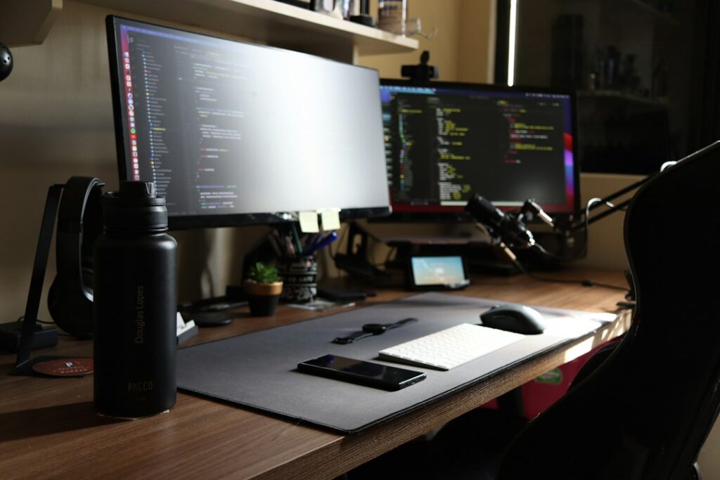 A developer’s desk with two monitors showing code, a keyboard, a mouse and a phone on a desk mat.
